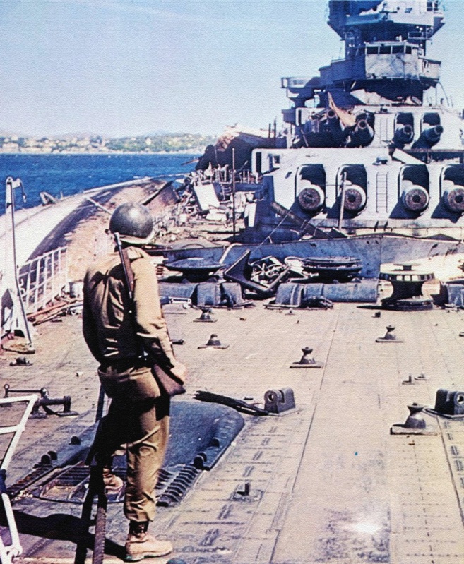 Американский солдат на палубе разрушенного французского линкора «Страсбург» (Strasbourg) в Тулоне. Рядом с линкором на боку лежит легкий крейсер «Ла Галиссоньер» (La Gallissoniere)..jpeg