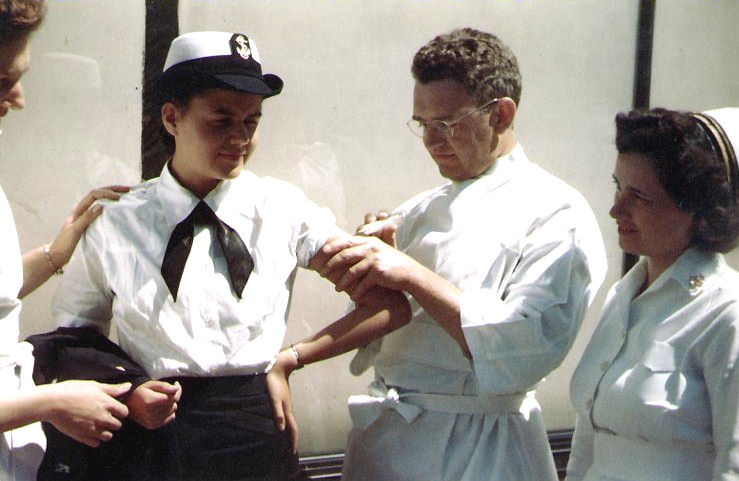 A WAVE gets her (shots) from a Navy doctor, as nurses stand by. Photographed prior to January 1945..jpg